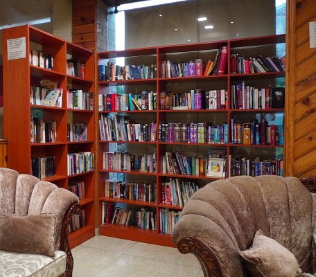 Cozy library reading corner with wooden bookshelves and plush armchairs at Ojaswi Resort.